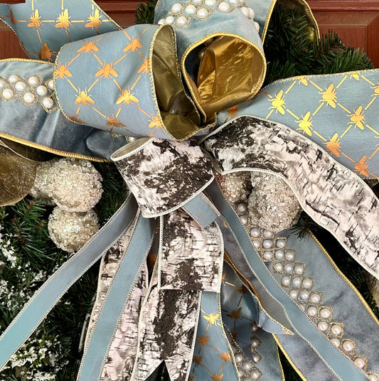 Decorative bow with blue, gold, and silver ribbons on a Christmas tree.