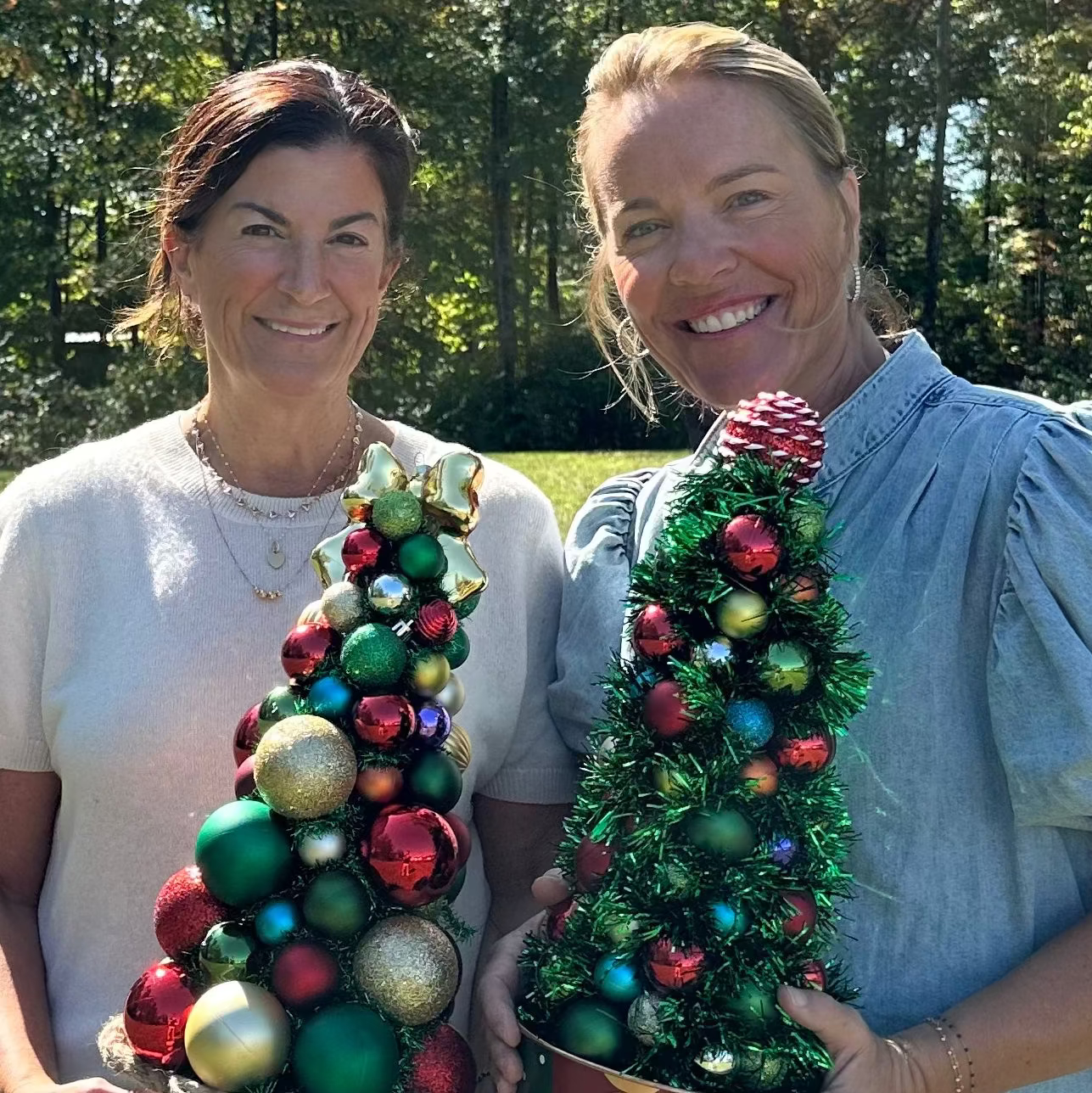 Two women holding decorative Christmas trees outdoors.