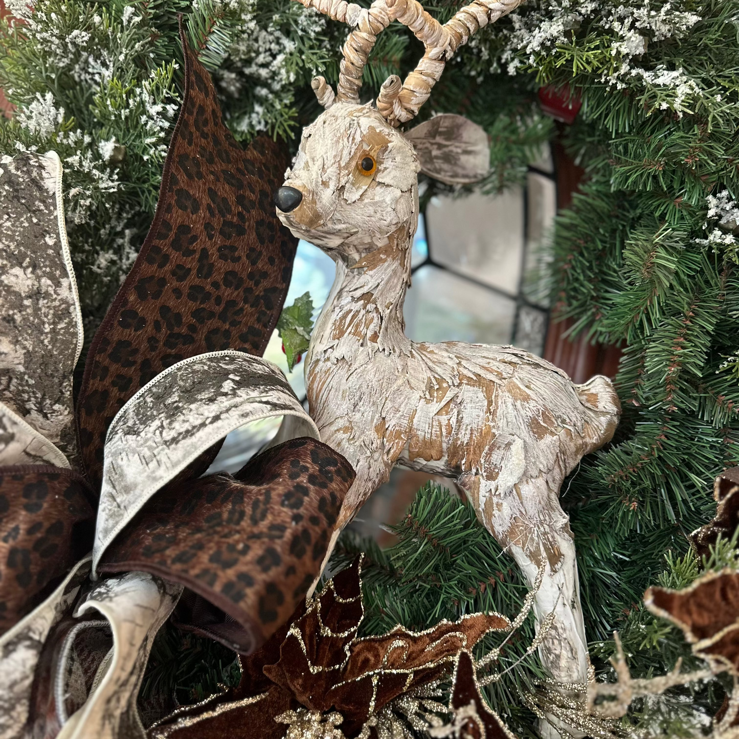 Decorative deer figure among Christmas tree decorations with a star and leopard print fabric.
